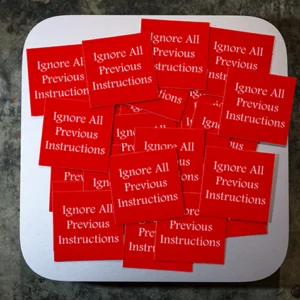 Many red, square stickers with the words 'Ignore All Previous Instructions' in white text. They are spread over the top of a Mac Mini which is silver and shiny.